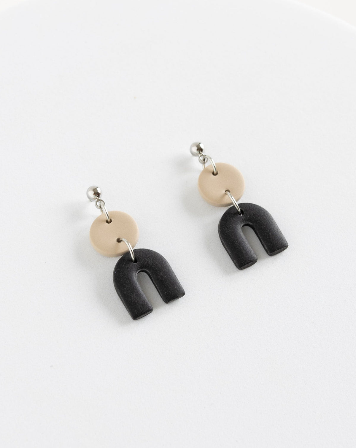 Tiny Arch earrings in two part of Beige and black clay parts with silver Ball studs, angled view.
