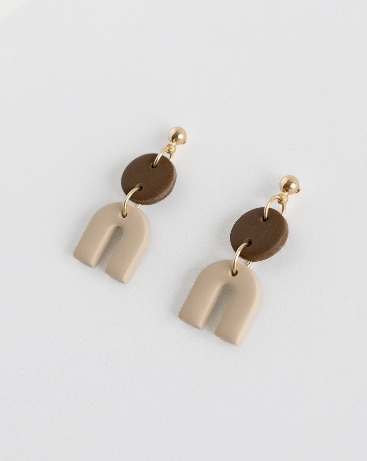 Tiny Arch earrings in two part of brown and beige clay parts with gold plated Ball studs, angled view.