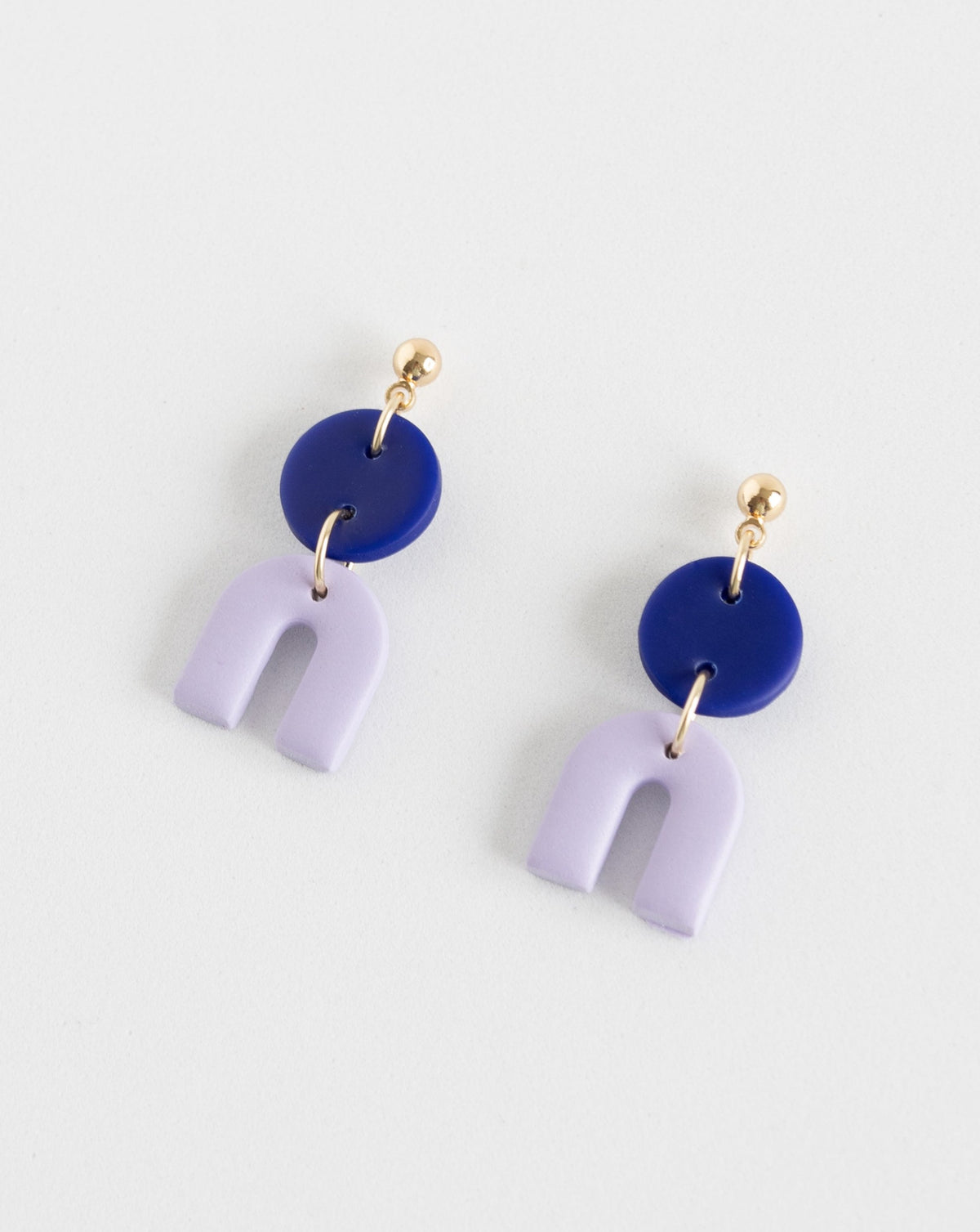 Angled view of Tiny Arch earrings in two part of Hue Blue and lilac  clay parts with Gold plated Ball studs.