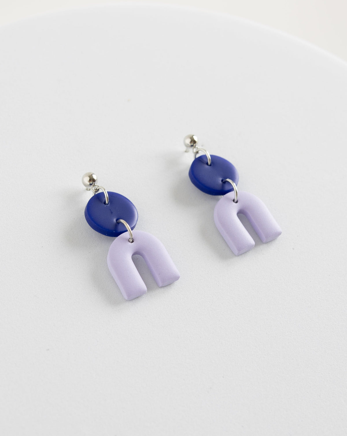 Tiny Arch earrings in two part of Hue Blue and lilac  clay parts with silver Ball studs, angled view.