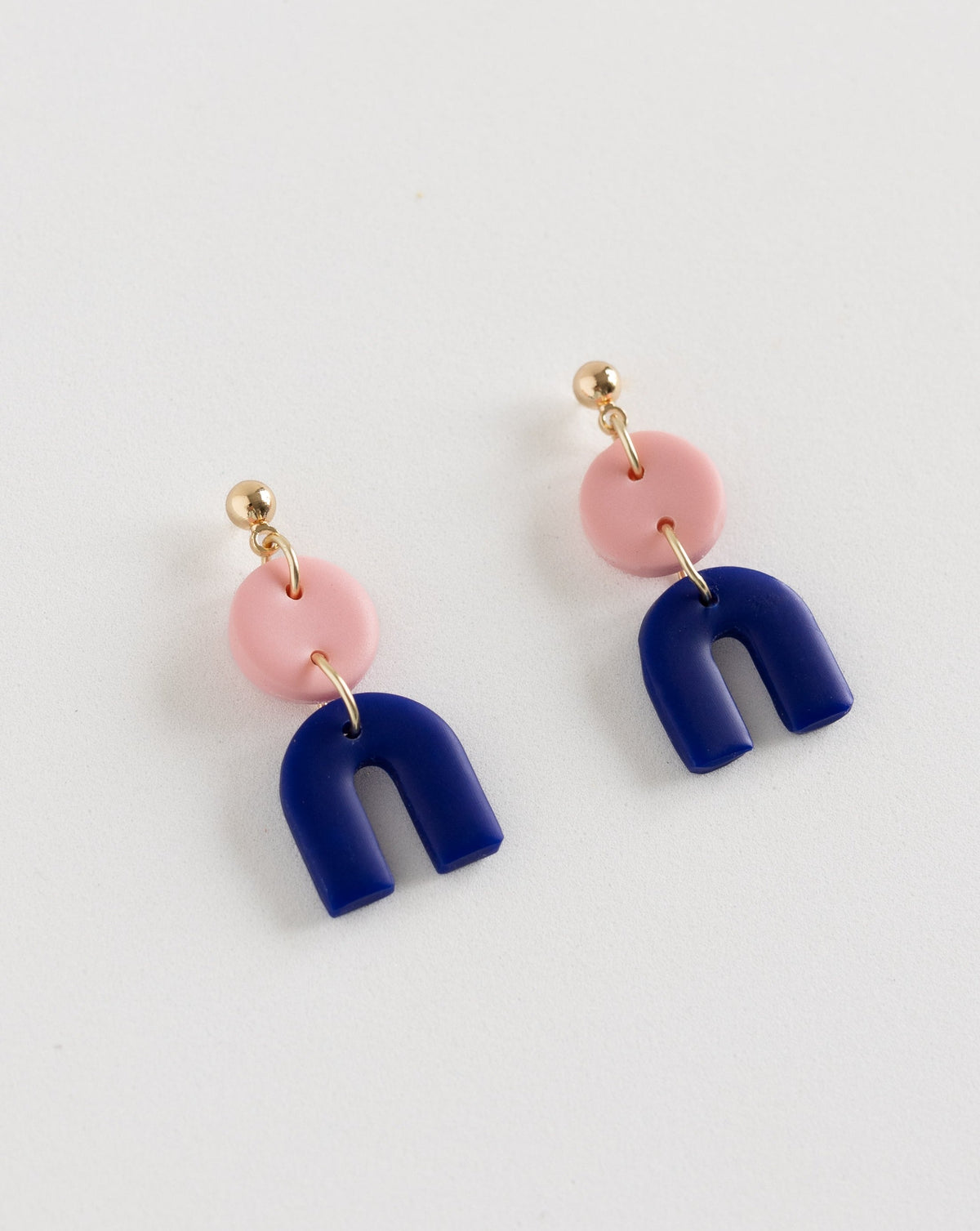 Tiny Arch earrings in two part of Sof pink and Hue Blue polymer clay parts with Gold plated Ball studs, angled view.