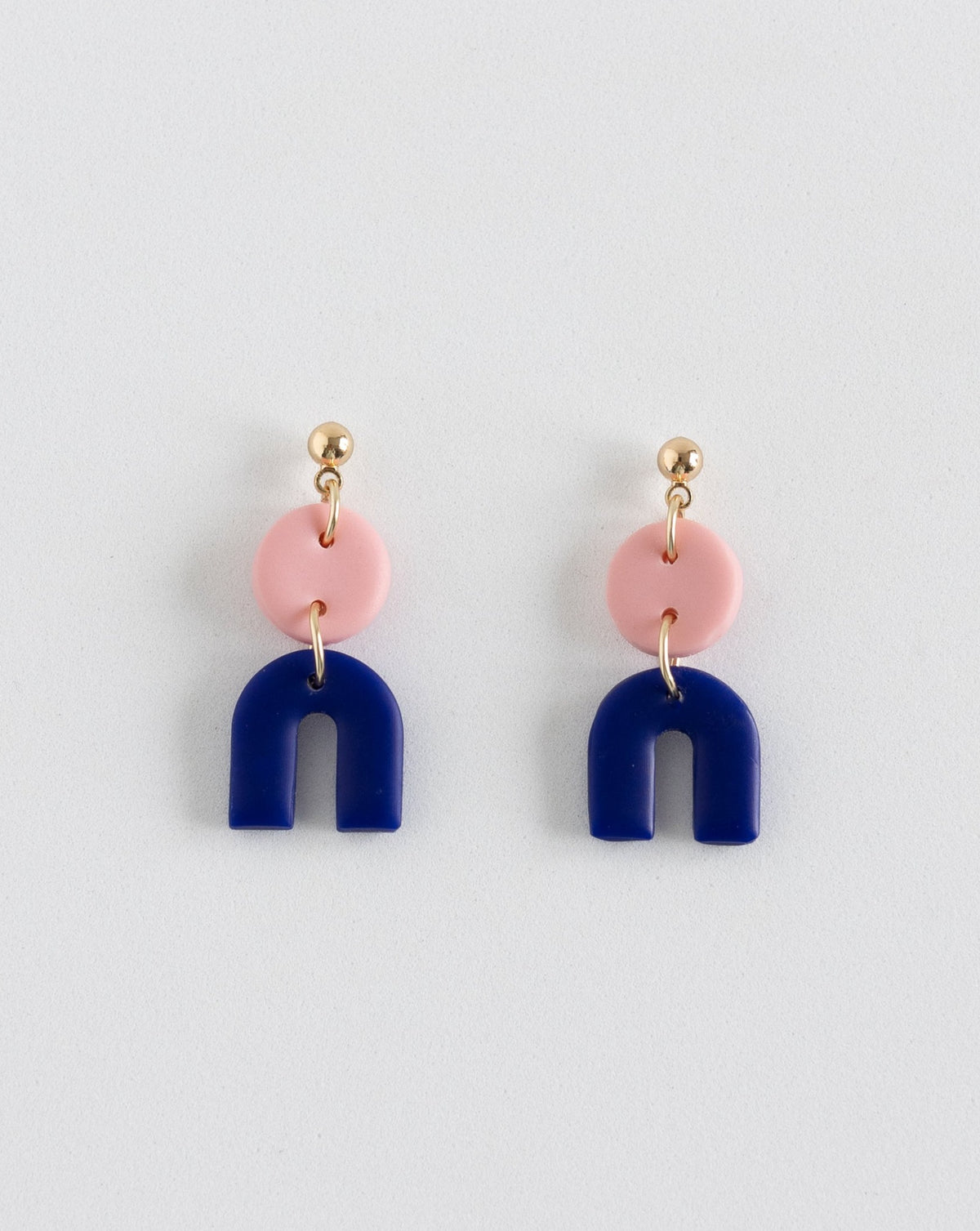 Playful &#39;Tiny Arch&#39; earrings, merging soft pink with hue blue clay, linked by gold plated studs, shown head-on.