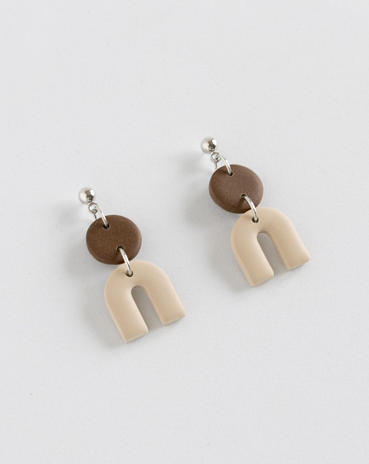 Tiny Arch earrings in two part of brown and beige clay parts with silver Ball studs, angled view.