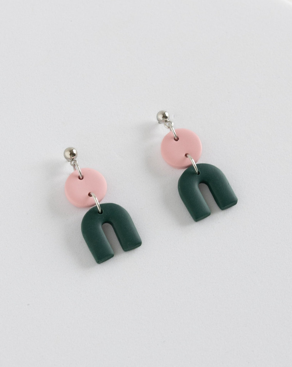 Tiny Arch earrings in two part of pink and pine clay parts with silver Ball studs, angled view.