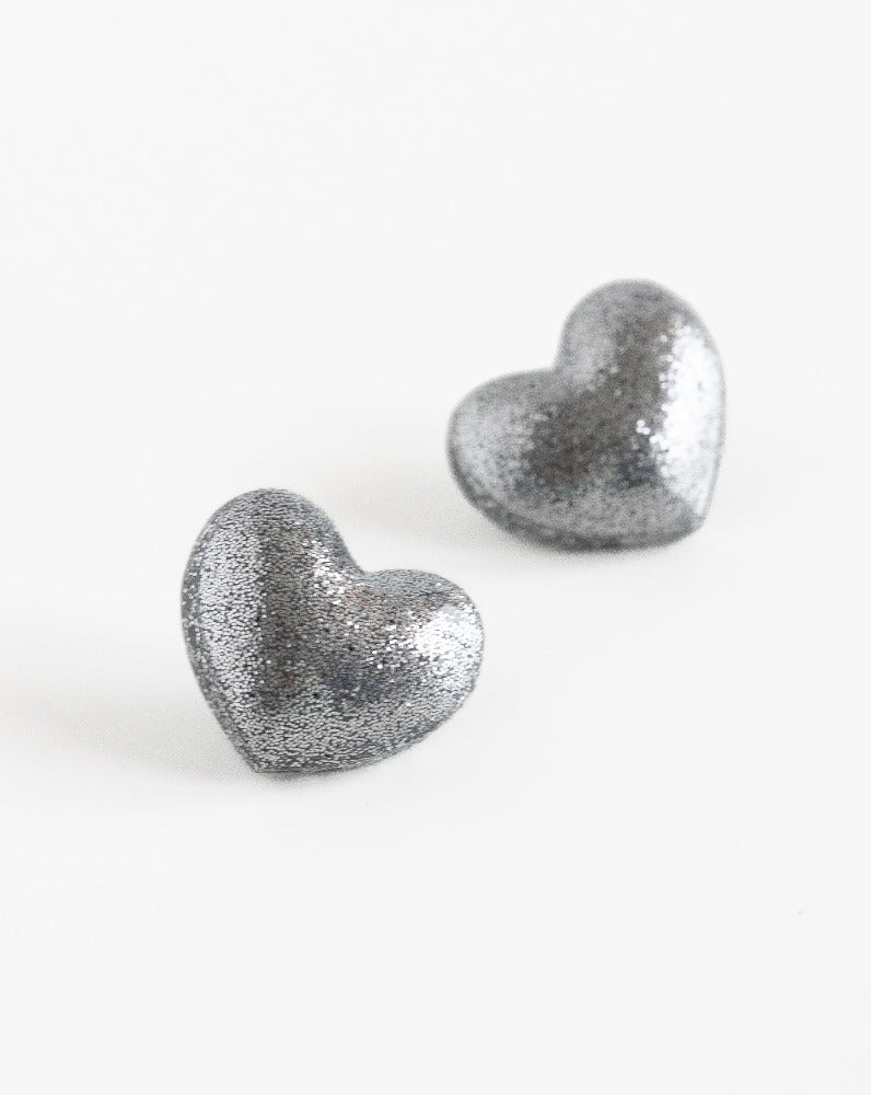 Close-up of heart stud earrings in shimmering silver color.