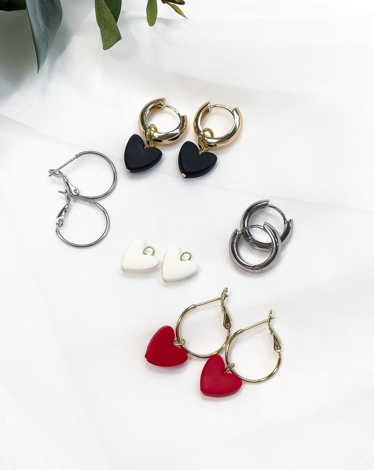 close up of Charming Heart collection with bold and regular hoops in silver and gold next to Heart charms in black, white and red colors. 