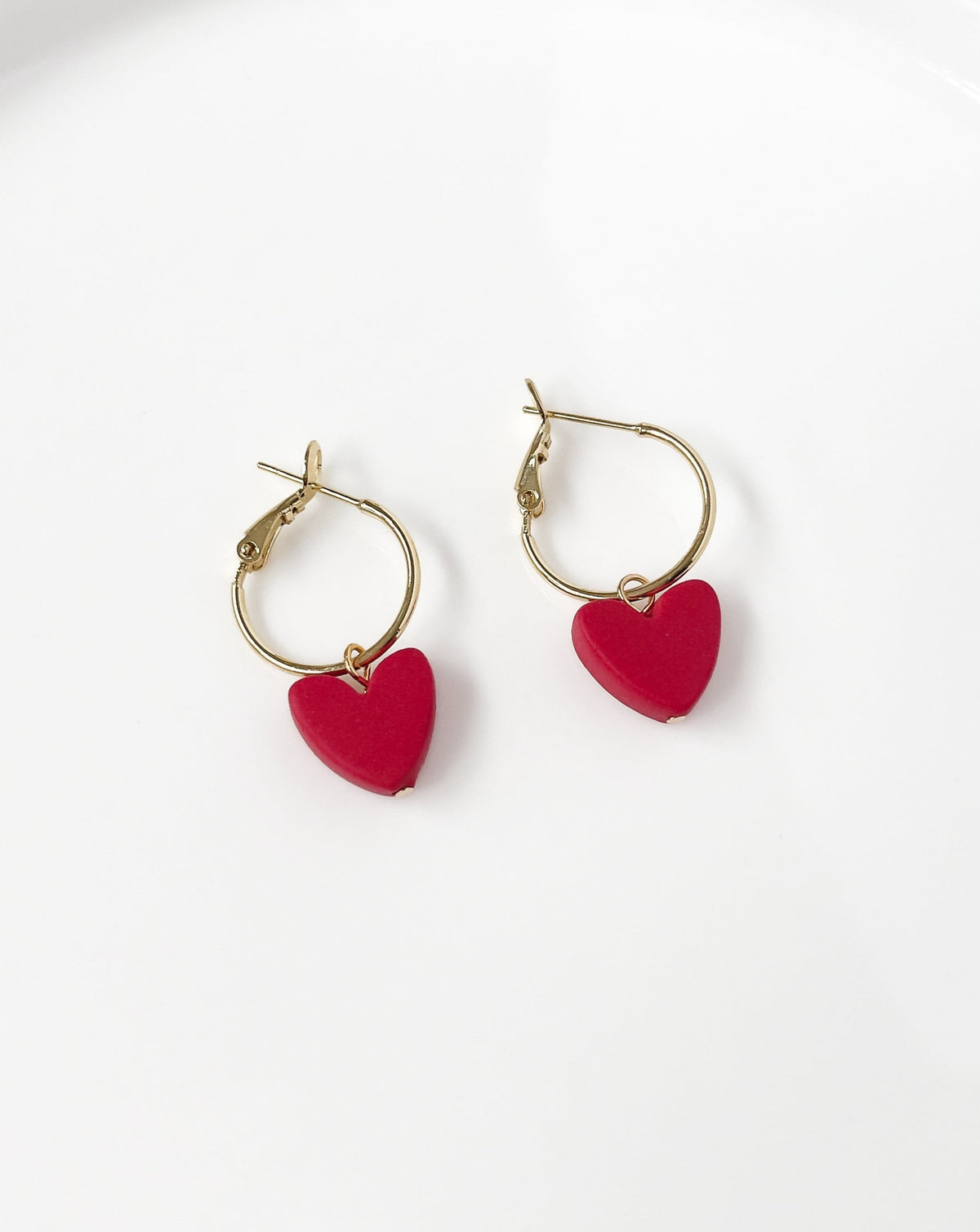 Angled view of Charming Heart earrings with Gold regular Hoops and Red Heart charm.