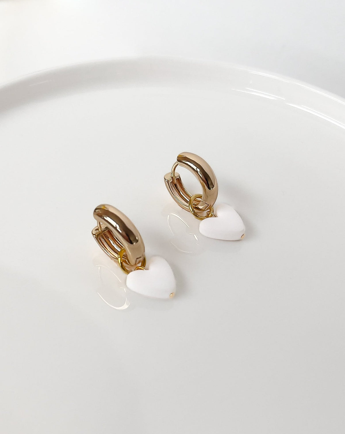 Angled view of Charming Heart earrings with Gold Hoops and White Heart charm.