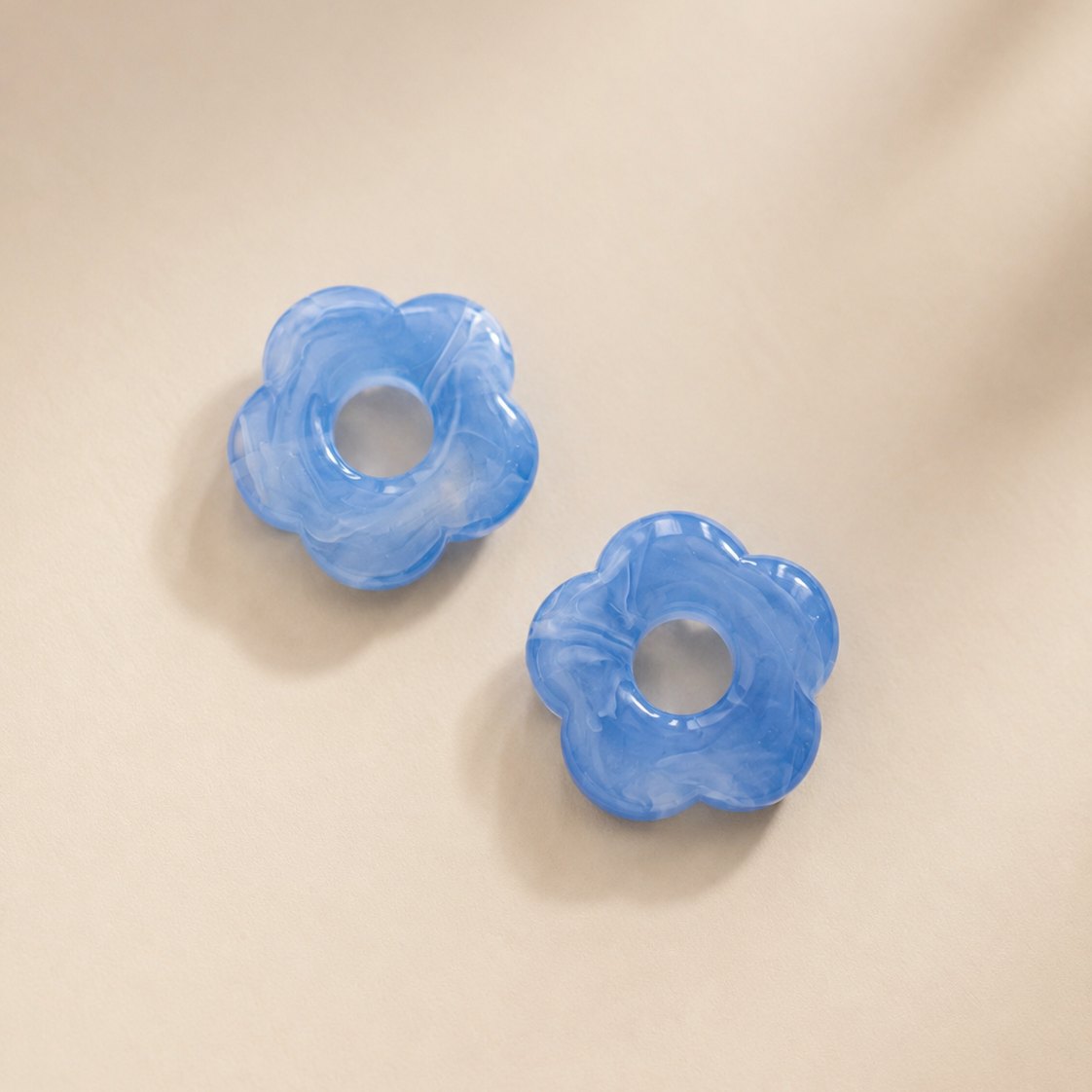 Two blue flower-shaped earring charm on a beige background